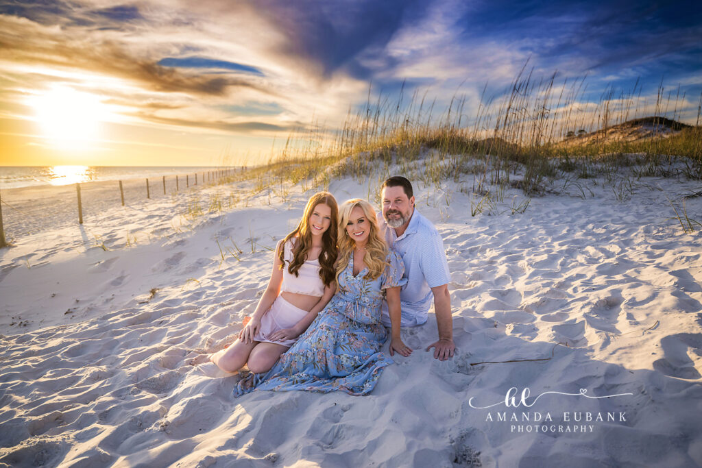A family seated on a sand dune with sea oats as sunbeams break through the clouds during a Bradenton family photography session