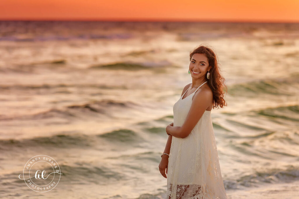 A senior girl in a white dress standing in the surf in soft golden light in Clearwater, Florida