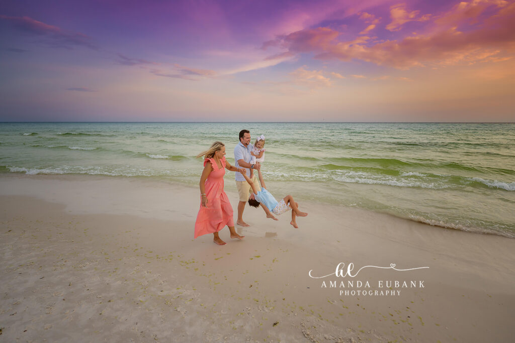 A mother in a coral dress with her children at the water's edge, photographed by a Holmes Beach family photographer