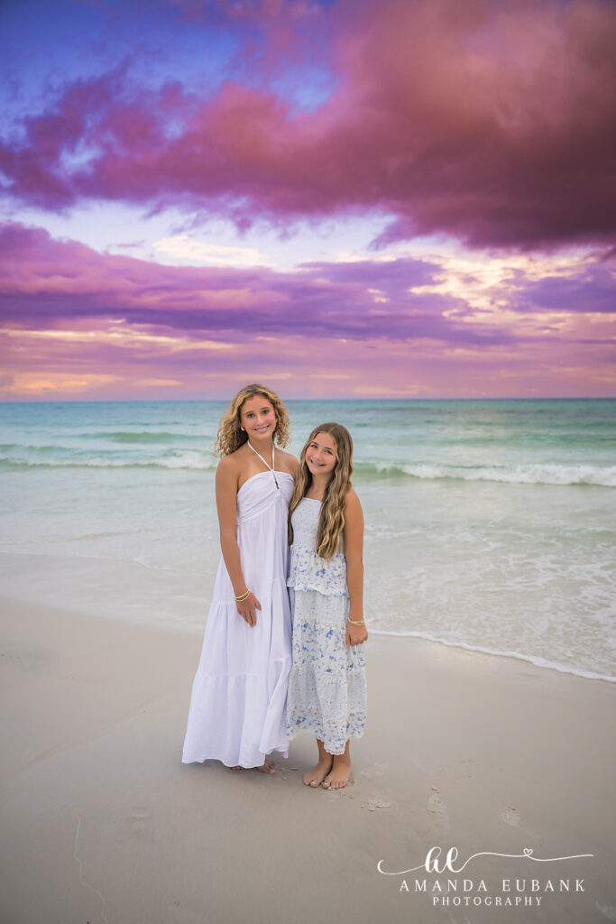 A mother and daughter in white dresses at the water's edge at sunset on Honeymoon Island, Florida
