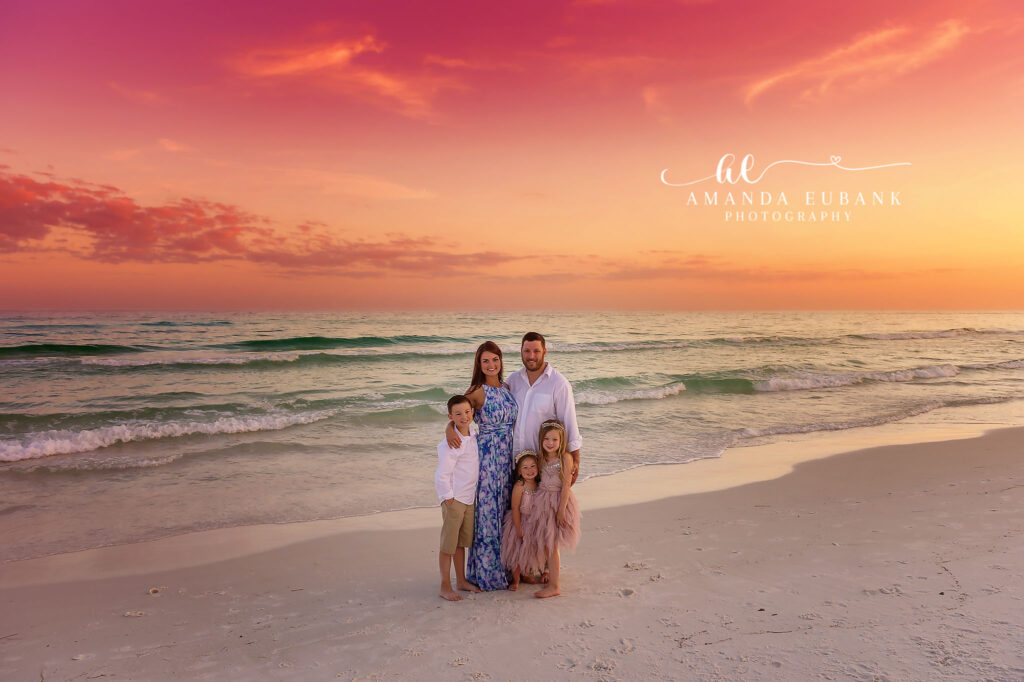 A family standing at the shoreline beneath an orange sunset, photographed by a Palm Harbor family photographer