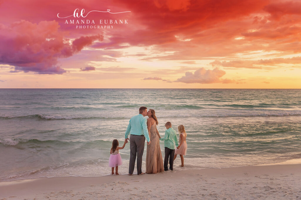 A family in mint and teal walking the shoreline beneath fiery clouds during a Palm Harbor family photography session