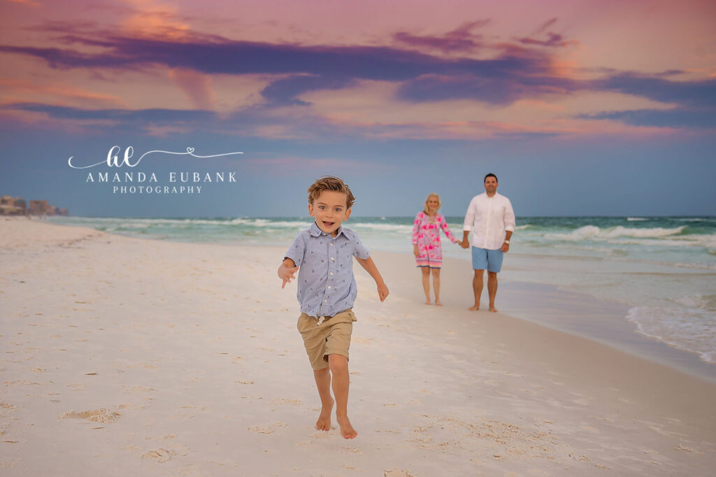 A little boy running down the beach ahead of his family in purple pastel light in Sarasota, Florida