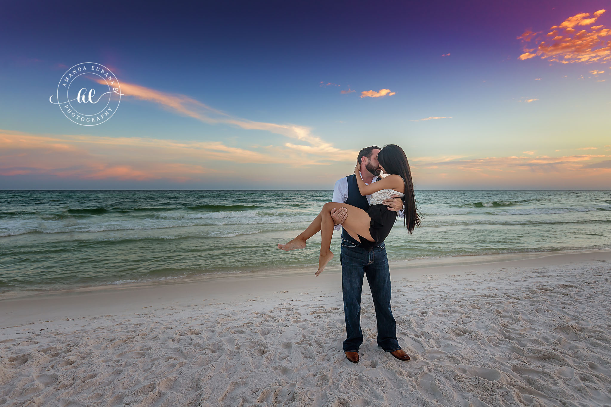 Carried Through the Sand at Dusk | Tampa Engagement Photographer A man carrying his fiancee in his arms across the sand beneath a violet and rose sky during a Tampa engagement photography session.