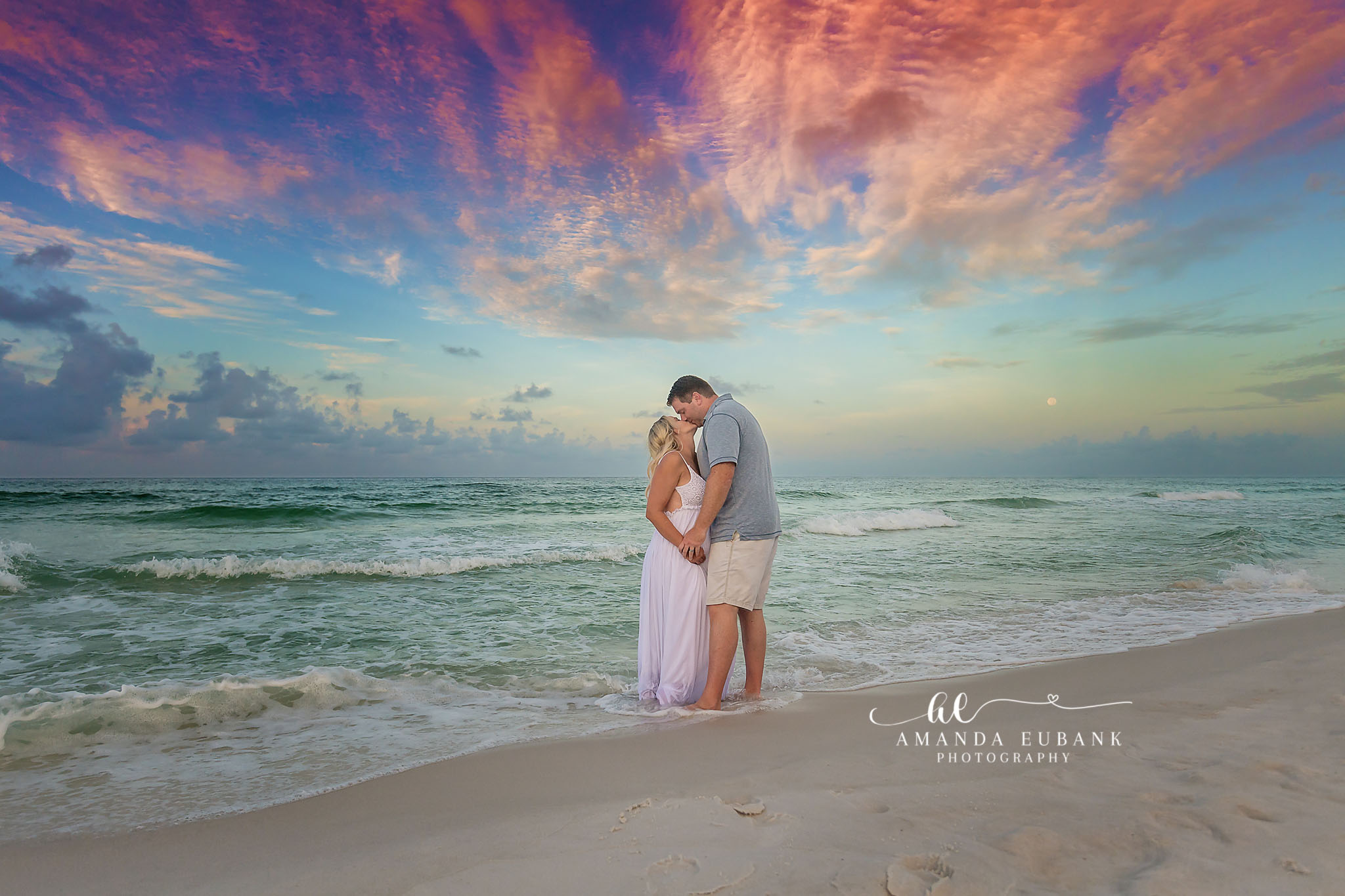 Embrace Beneath a Painted Sky | Tampa Beach Engagement Photography Tampa engagement photographer captures a couple wrapped in an embrace on the beach under vivid pink and blue sunset clouds.