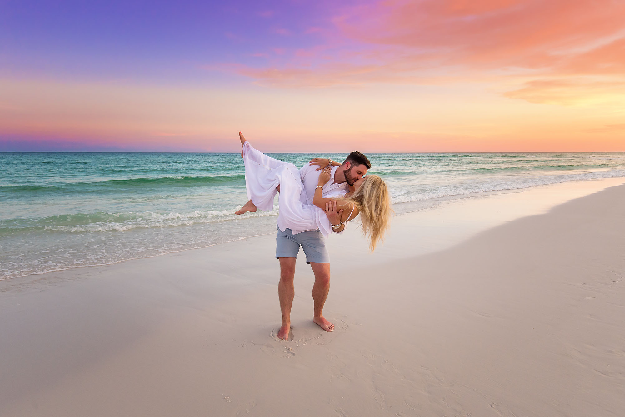 Twirling in the Sand | Tampa Engagement Photographer A man spinning his fiancee across the sand as pastel light spreads over the Gulf during a Tampa engagement photography session.