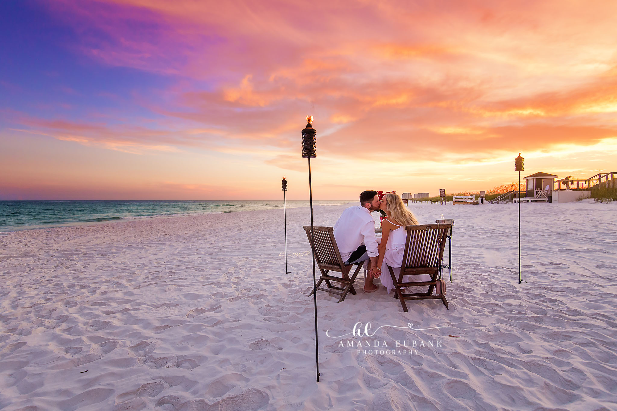 Tiki Torch Sunset Session | Tampa Beach Engagement Photography Tampa engagement photographer captures a couple seated in beach chairs between lit tiki torches as the sky burns orange.