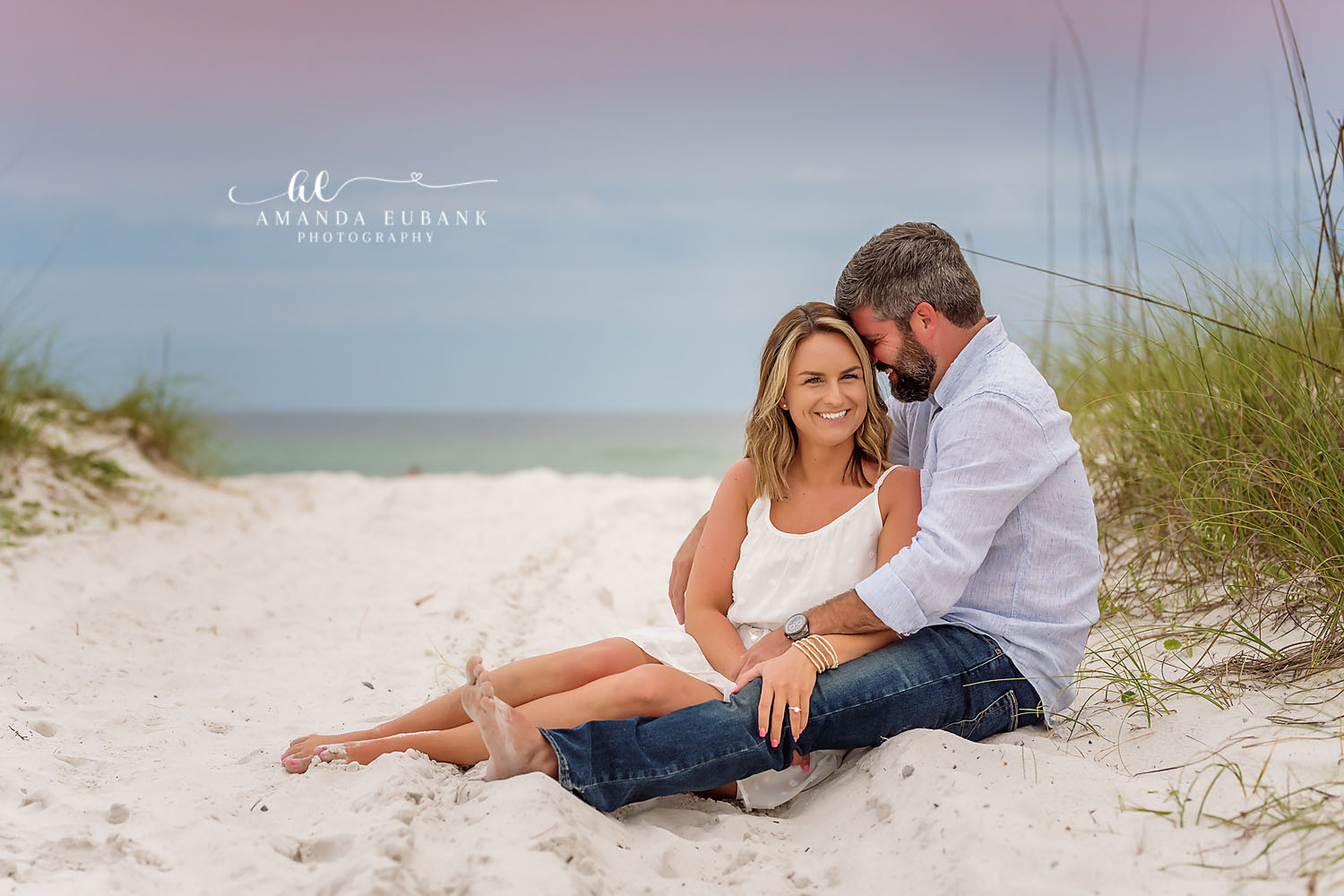 Laughing in the Sand Dunes — Tampa, FL Engagement Session An engaged couple laughing together on the sand beside tall dune grass at a Gulf beach engagement session near Tampa, Florida.