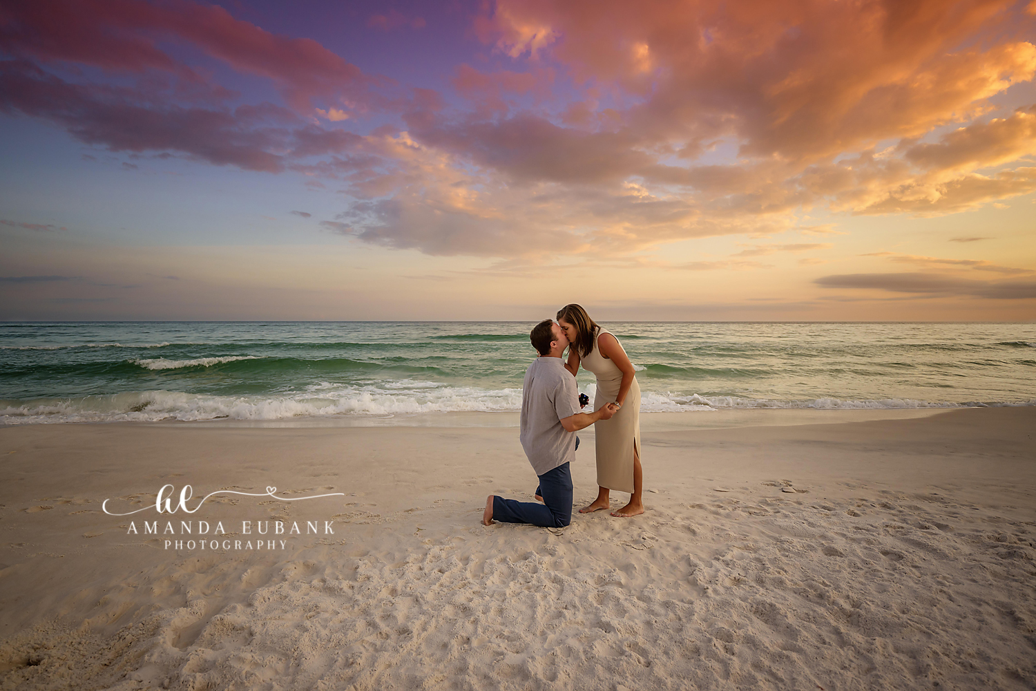 The Question on the Sand | Tampa Engagement Photographer A man on one knee proposing on the sand beneath streaks of gold sunset cloud during a Tampa engagement photography session.