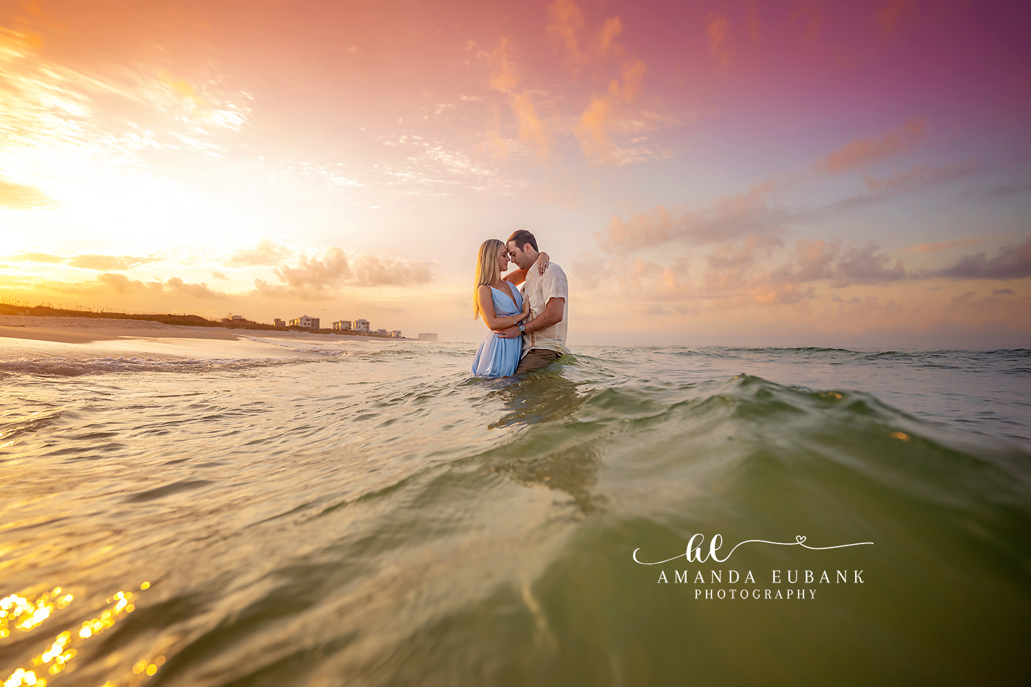 Waist-Deep at Sunset — Tampa, FL Engagement Session A couple holding one another waist-deep in the Gulf as the sun bursts through cloud at a Gulf beach engagement session near Tampa, Florida.