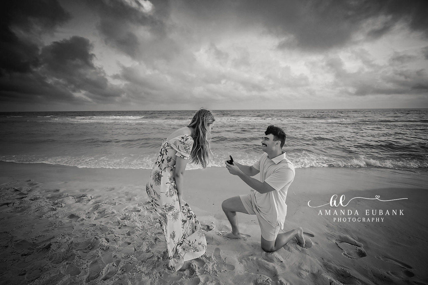 Monochrome Proposal — Tampa Bay Engagement Photography A black and white frame of a proposal on the sand beneath heavy clouds — beach engagement photography in Tampa Bay.
