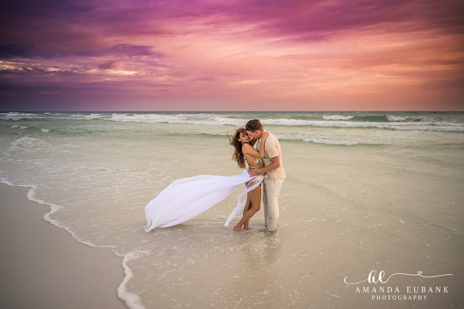 Embrace in the Surf | Tampa Engagement Photographer A couple embracing in the surf, her gown floating under lavender and coral light during a Tampa engagement photography session.