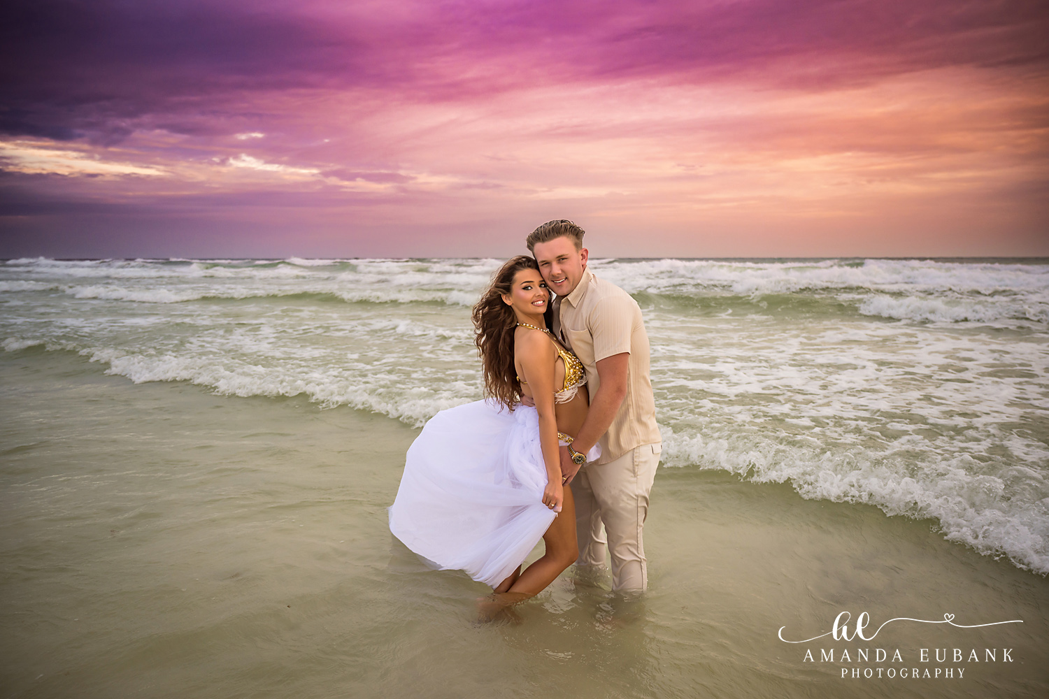 Waves and a White Gown — Tampa, FL Engagement Session A couple holding each other as waves roll past her drifting white gown at a Gulf beach engagement session near Tampa, Florida.
