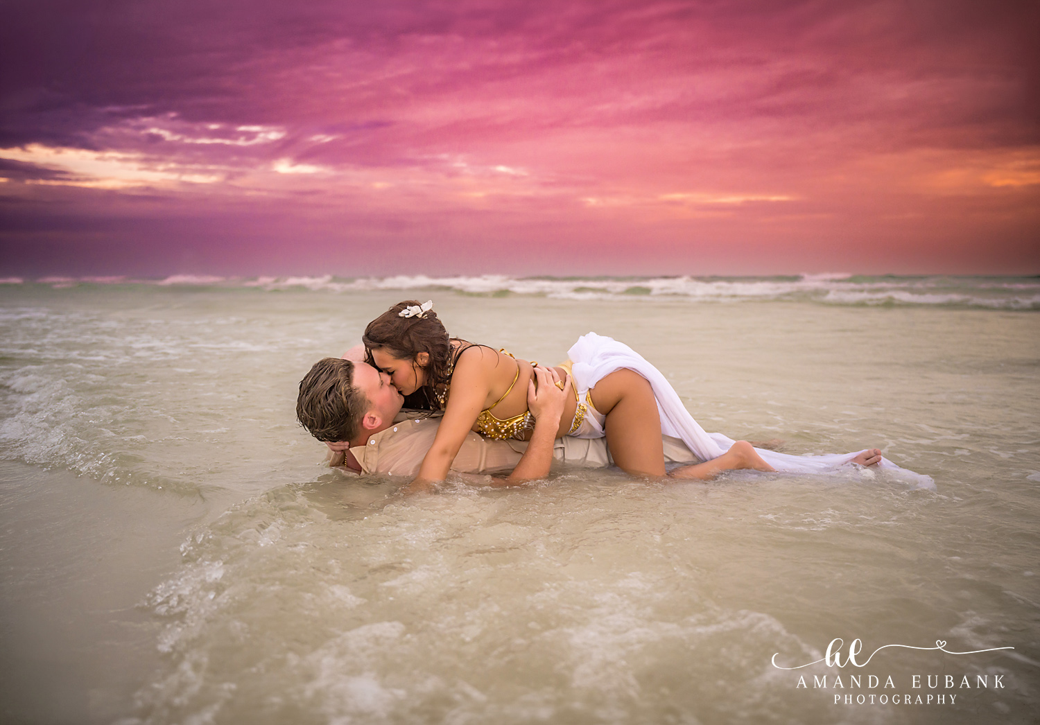 Kissing as the Wave Washes In — Tampa, FL Engagement Session A couple kissing in the shallows as a wave washes over them at a Gulf beach engagement session near Tampa, Florida.