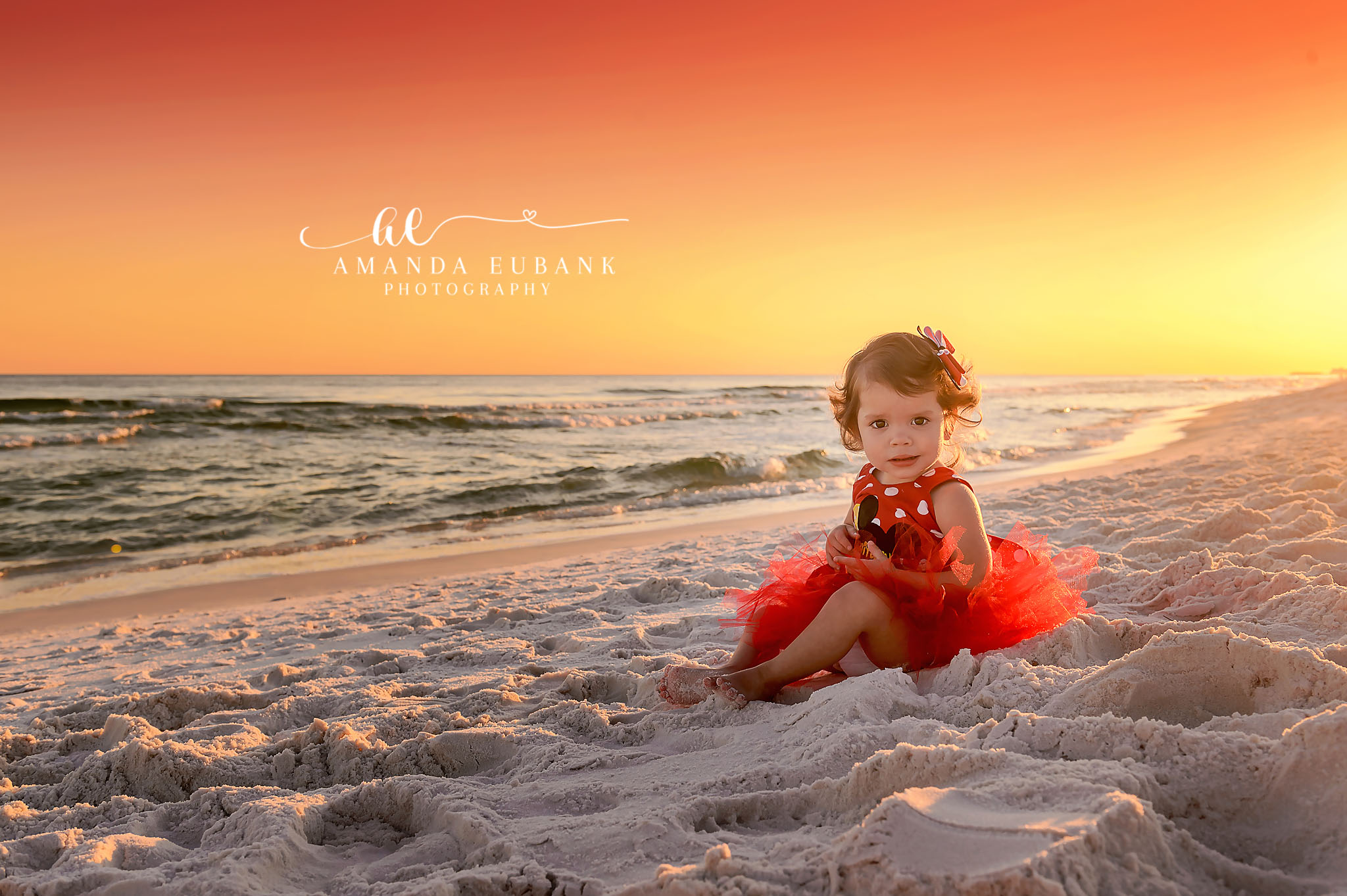Toddler in a Red Tutu | Tampa Children’s Photographer A toddler girl in a red tutu sitting on the sand in golden sunset light during a children’s portrait session in Tampa, Florida.