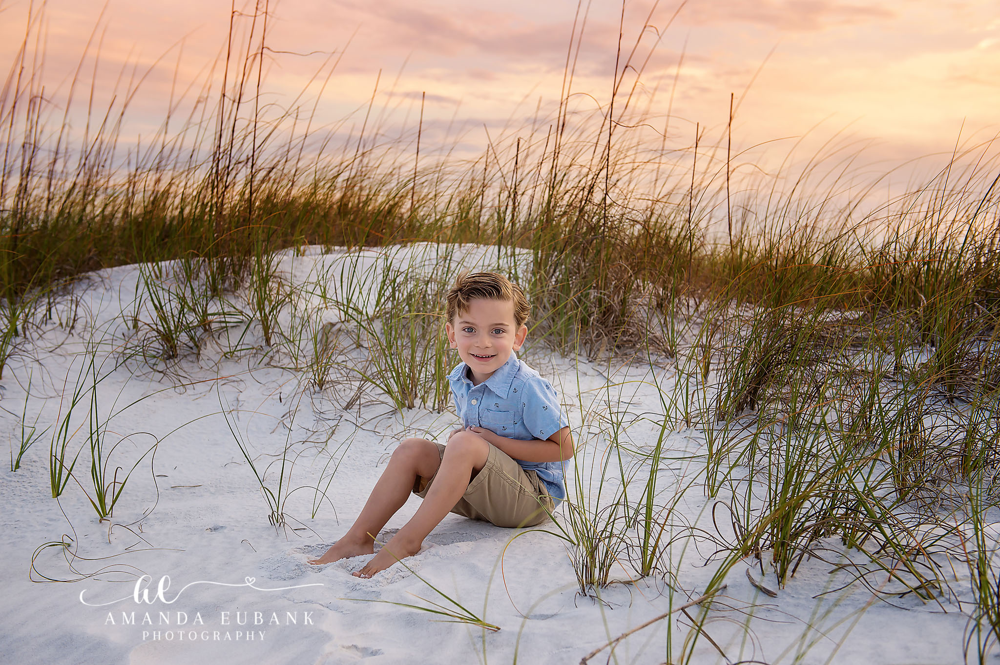 Little Boy in the Dunes | Kids Beach Portraits in Tampa, FL Tampa children’s photographer captures a young boy in a blue polo sitting on a white dune among the sea oats.