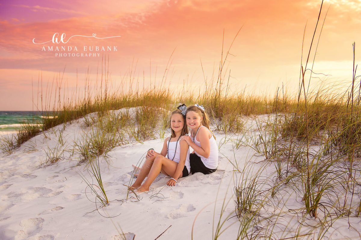 Sisters in the Dunes | Tampa Children’s Photographer Two sisters sitting together in the dunes as the sea oats glow gold during a children’s portrait session in Tampa, Florida.
