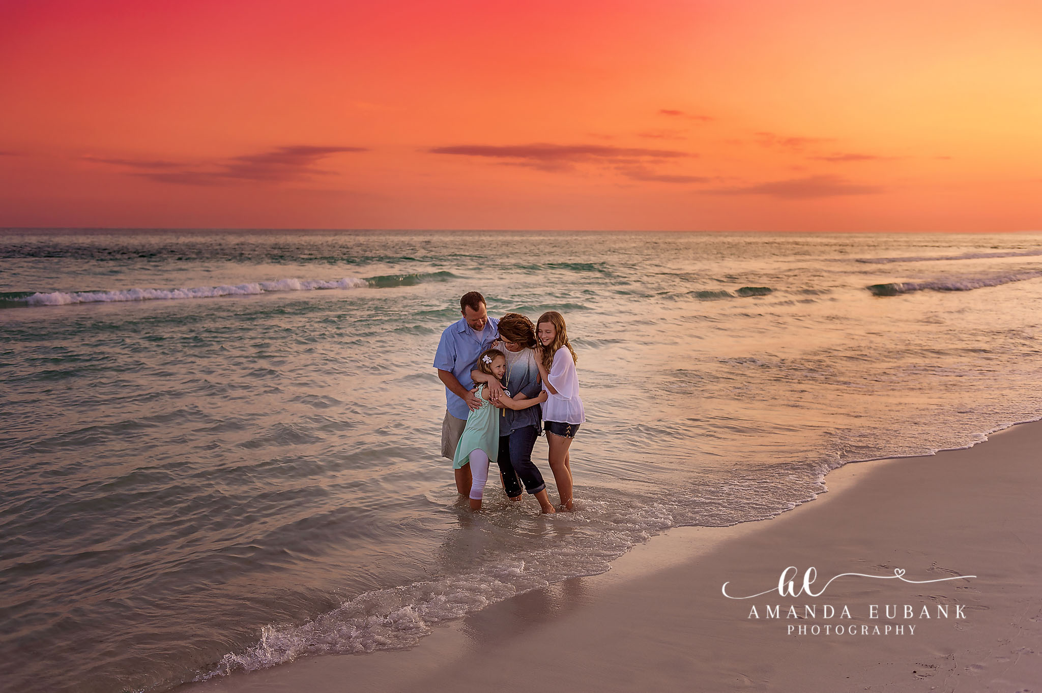 Family Embrace in the Surf | Tampa Beach Family Photography Tampa family photographer captures a family of four holding each other in the shallow surf under a coral sky.