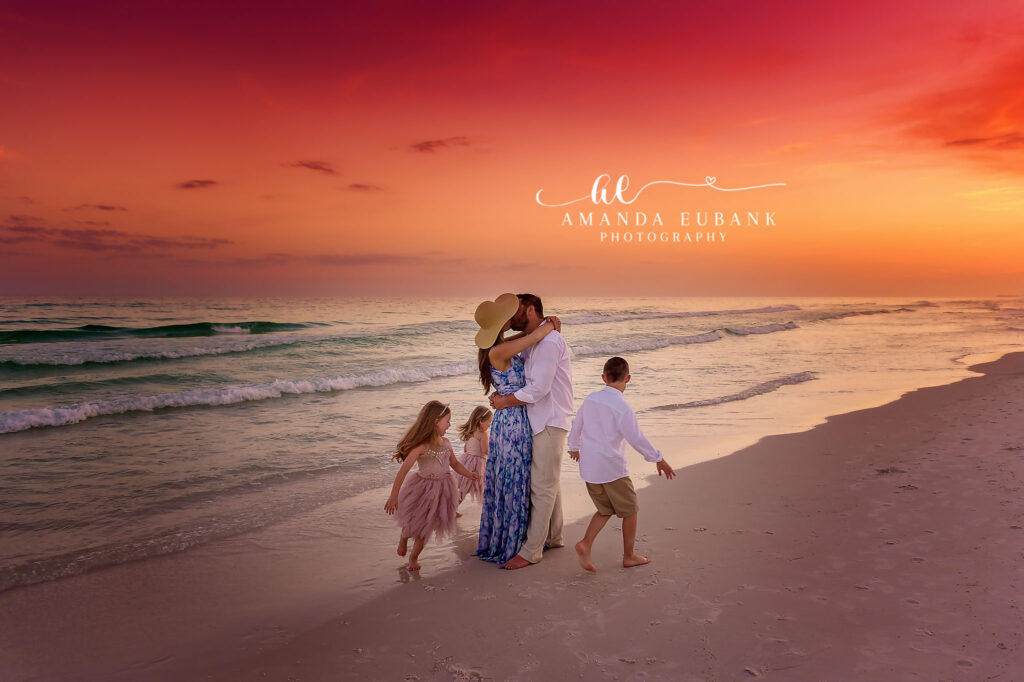 A family of four walking away along the shoreline beneath a crimson sky during a Tampa family photography session.