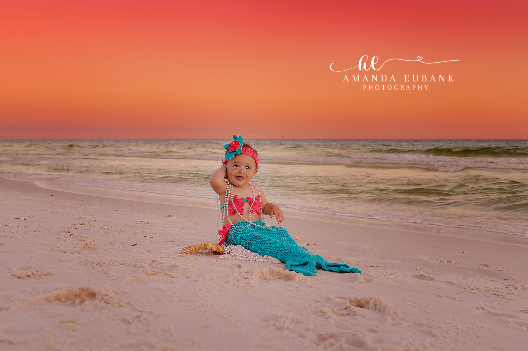Mermaid Tail Milestone — Tampa Bay Baby Photography A baby girl in a teal mermaid tail sitting on the sand at sunset at a beach milestone session in Tampa, FL.