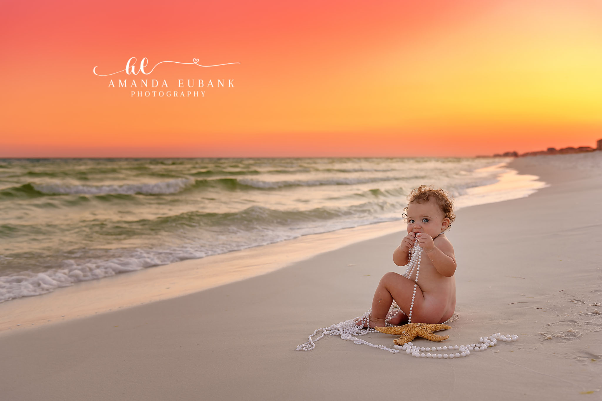 Baby at Sunset | Beach Milestone Photos in Tampa, FL Tampa baby photographer captures a baby sitting on the sand with hands to mouth under a vivid orange sky.