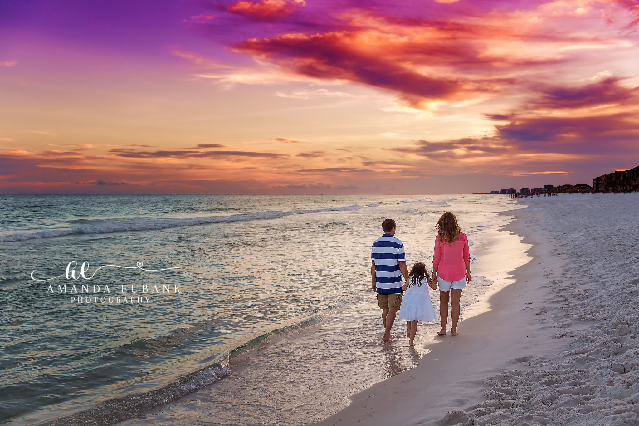 Mom and Kids at Dusk | Family Photographer in Tampa, Florida Family beach portraits in Tampa, FL showing a mother and two children walking away along the shoreline under purple clouds.