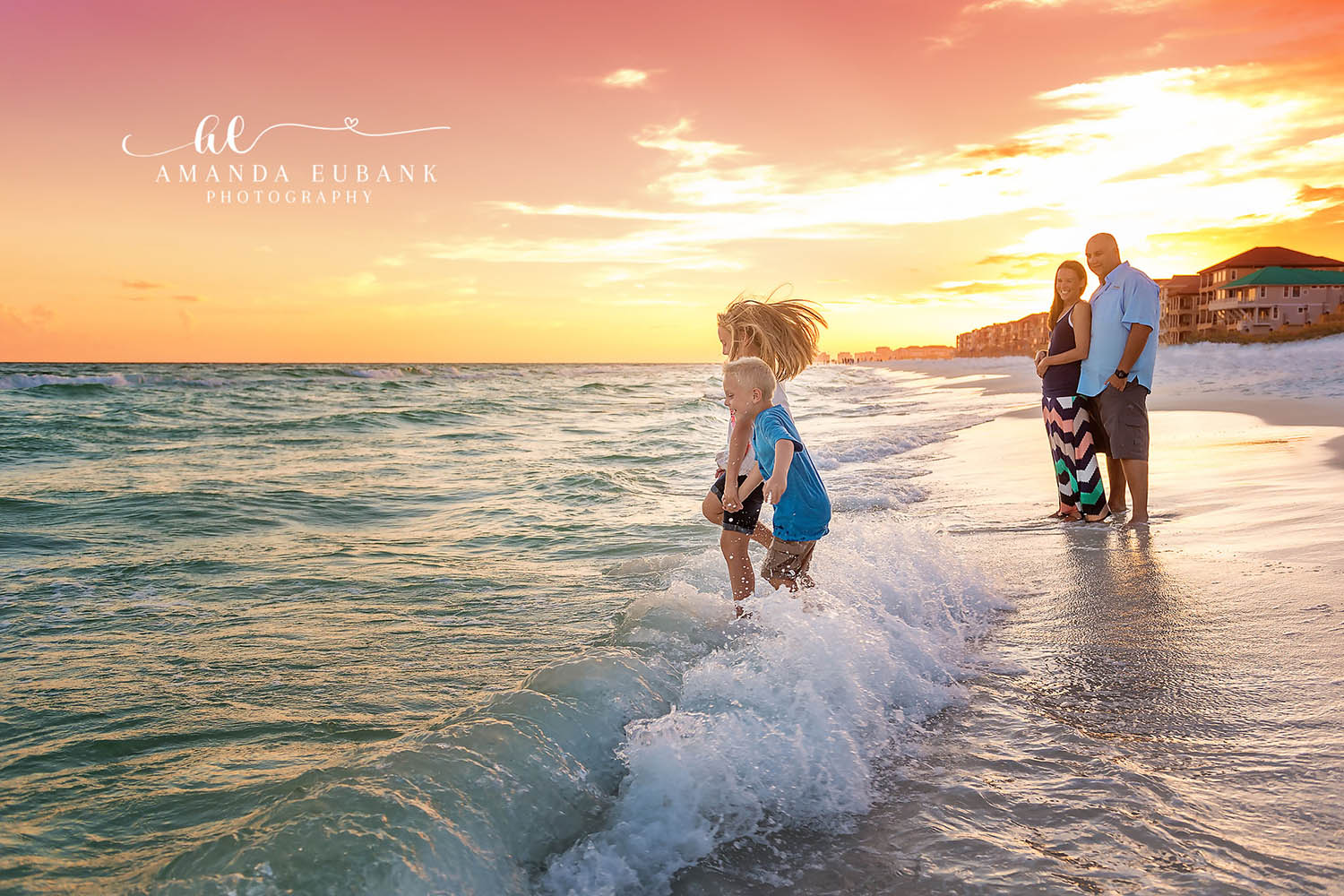 Playing in the Waves | Family Photographer in Tampa, Florida Family beach portraits in Tampa, FL showing children playing in a breaking wave while their parents watch at golden hour.