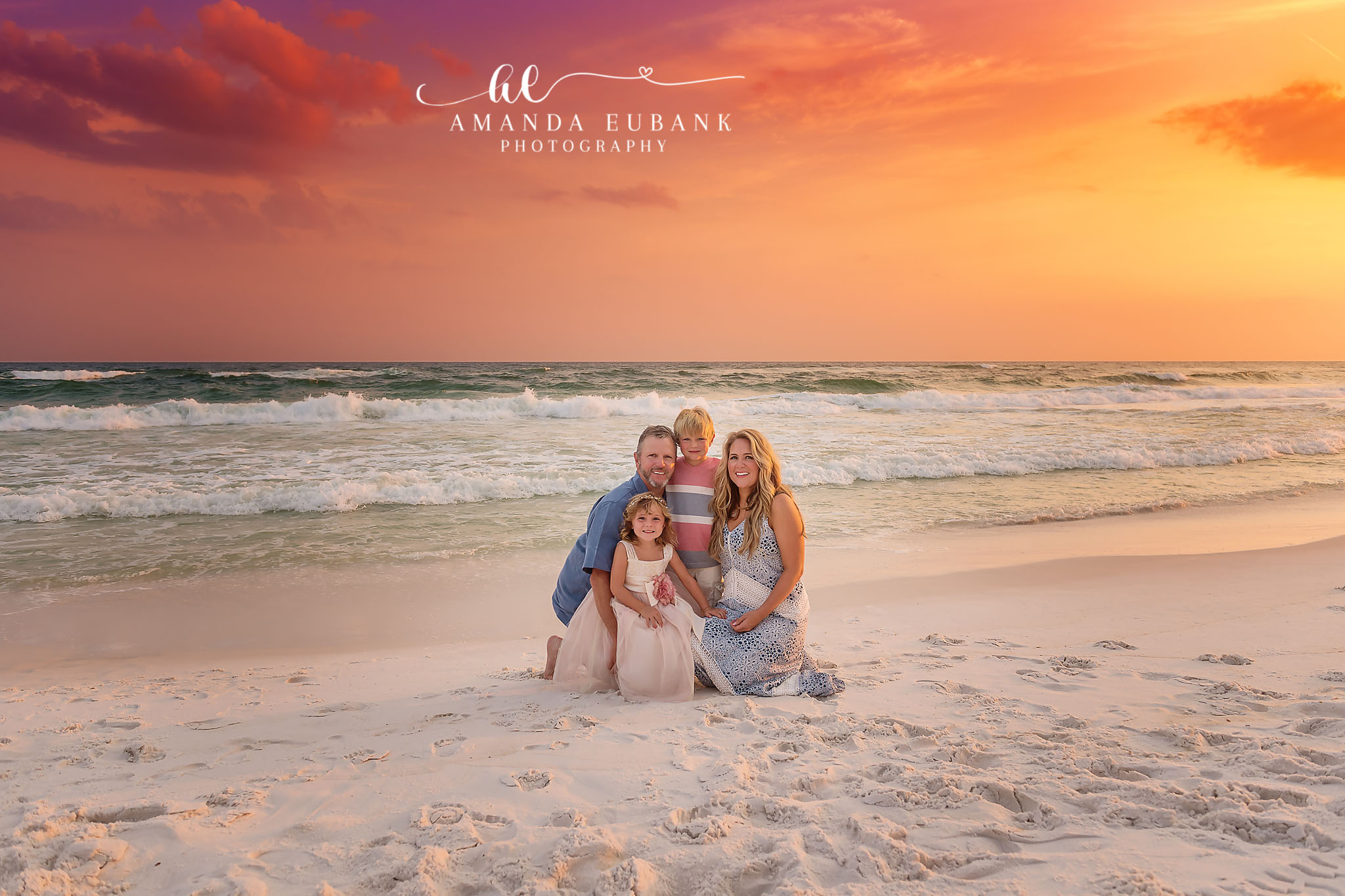 Family Kneeling in the Sand | Family Photographer in Tampa, Florida Family beach portraits in Tampa, FL showing a family of four kneeling together on the sand in denim and white at sunset.
