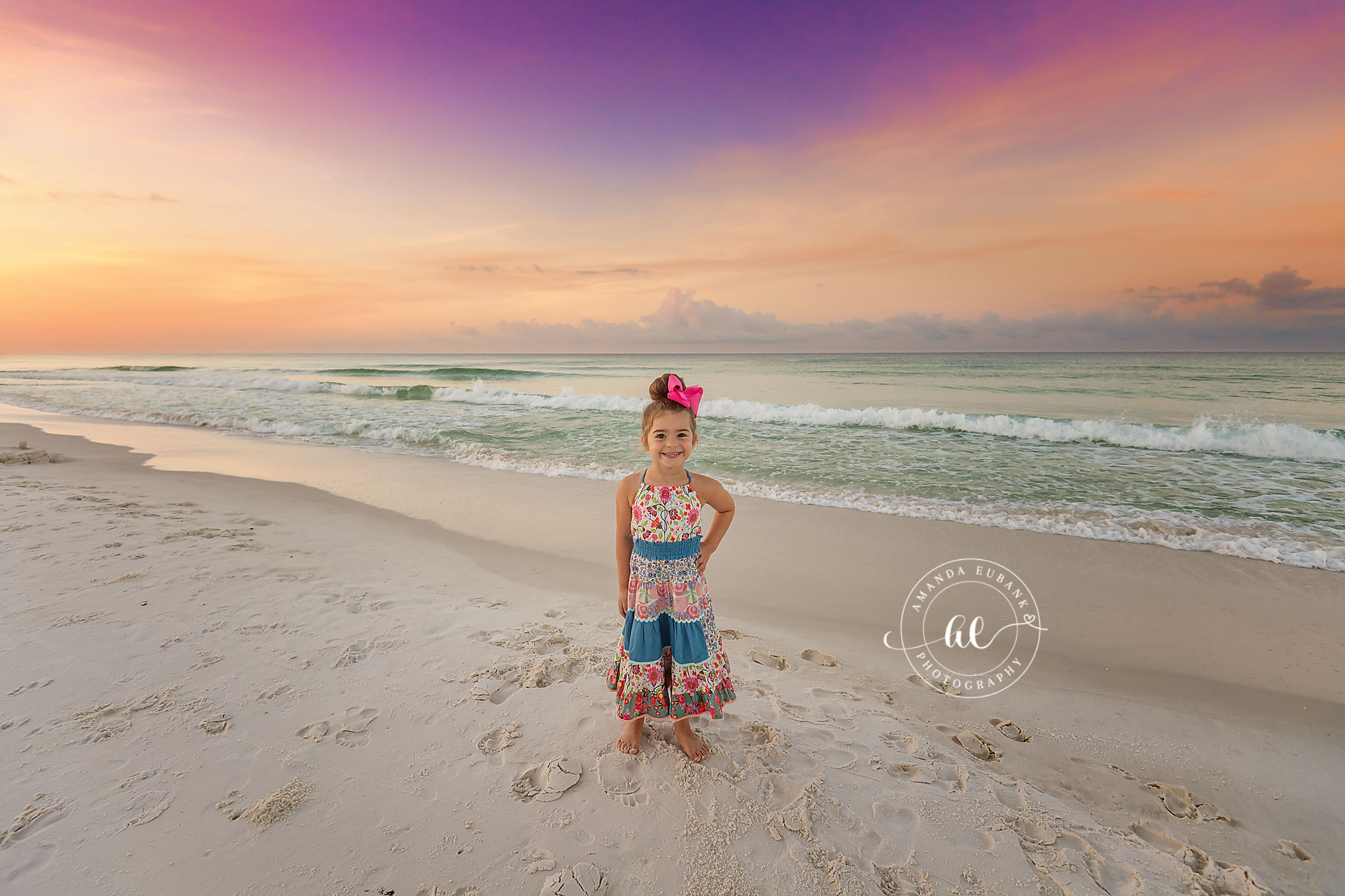 Little Girl on the Sand — Tampa Bay Children’s Photography A little girl in a floral dress standing on the sand under a pastel sky at a beach kids session in Tampa, FL.