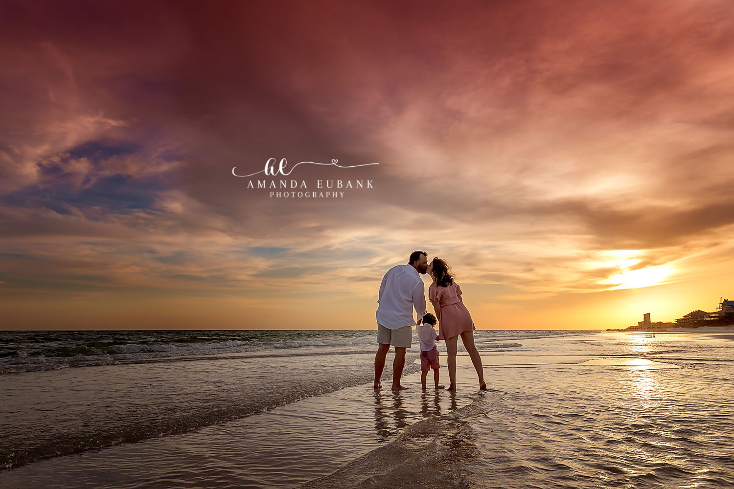 Storm Light Silhouette — Tampa, FL Family Session A family of three silhouetted at the shoreline under dramatic golden storm light at a beach family session near Tampa, Florida.