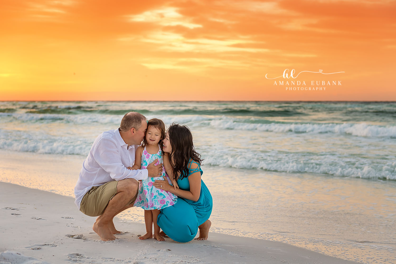 Cheek Kiss on the Sand — Tampa, FL Family Session Parents crouched beside their daughter as dad kisses her cheek at golden hour at a beach family session near Tampa, Florida.