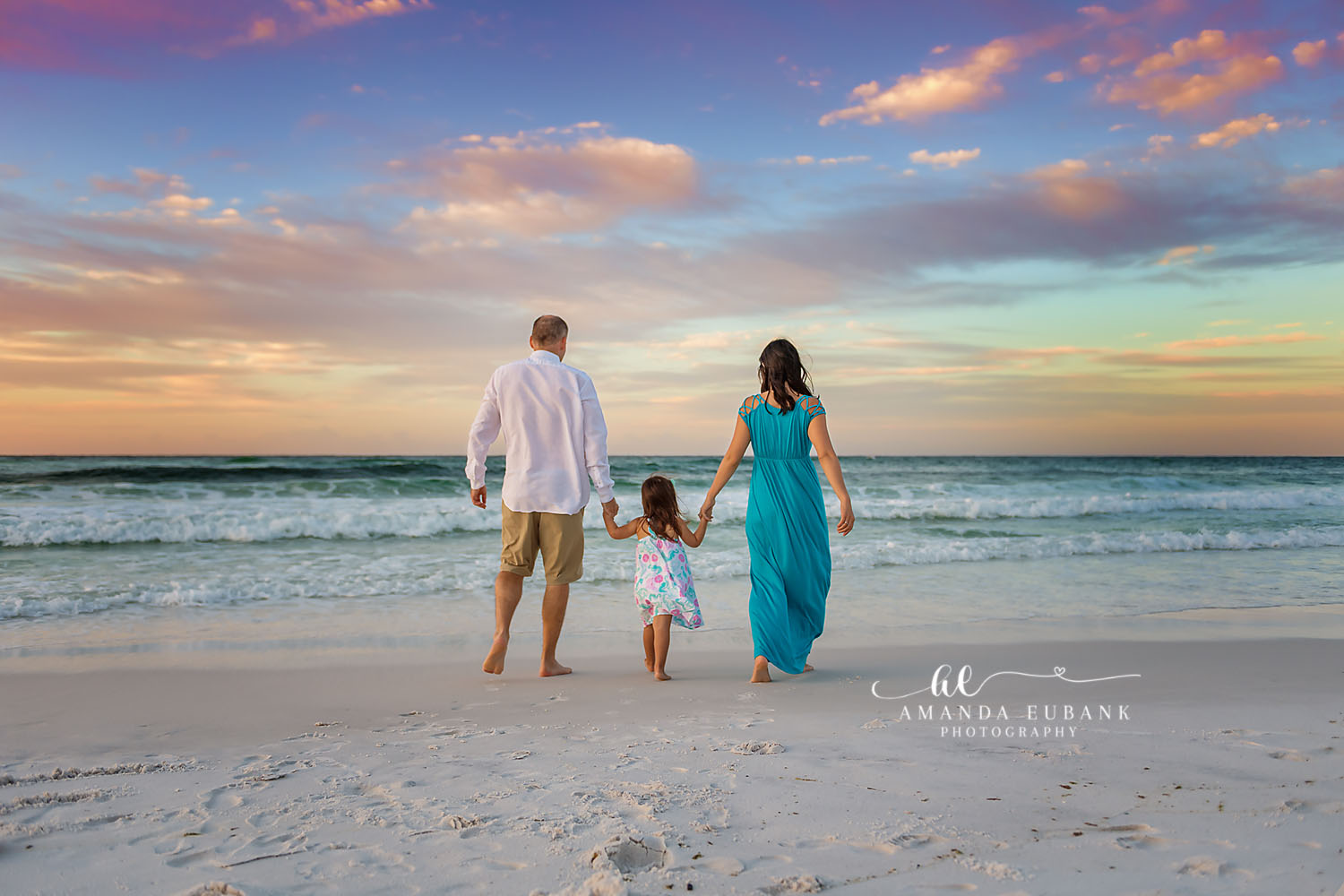 Wide Sky Family Walk | Family Photographer in Tampa, Florida Family beach portraits in Tampa, FL showing a family of three walking the wet sand beneath a wide pastel sky.