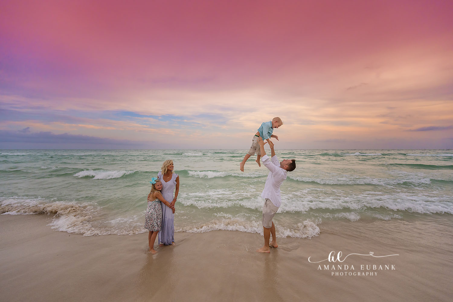 Baby in the Air | Family Photographer in Tampa, Florida Family beach portraits in Tampa, FL showing a dad tossing his baby into the air in the surf while mom watches.