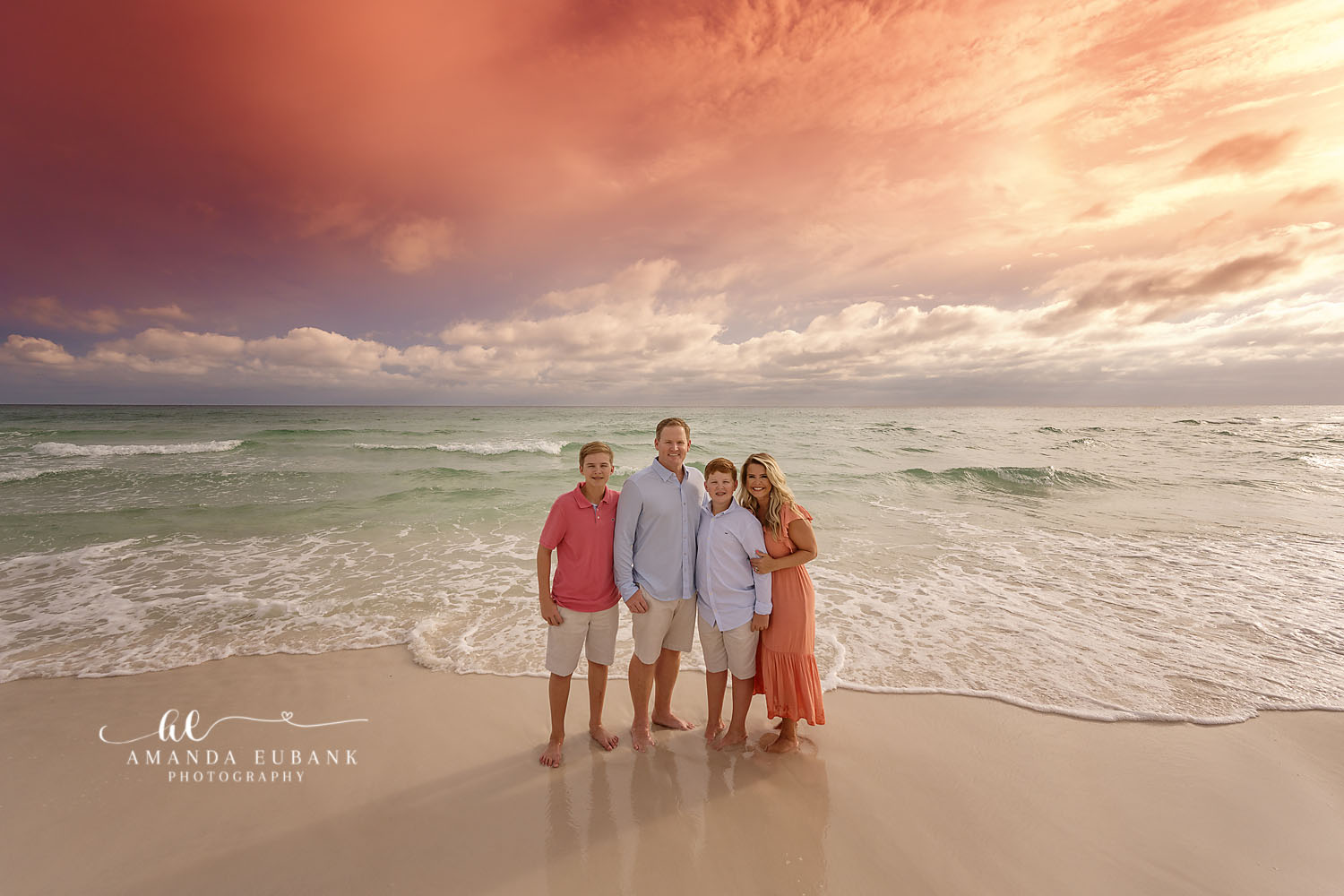 Family in Coral and Blue | Tampa Beach Family Photography Tampa family photographer captures a family of five standing on wet sand in coral and blue under pastel clouds.