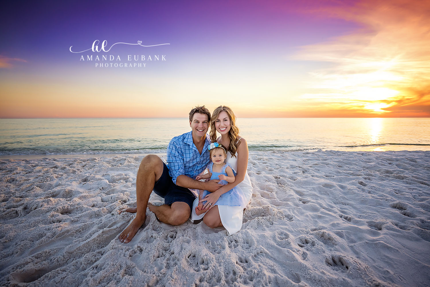 Sitting With the Toddler | Tampa Family Photographer A family of three sitting on the sand with their toddler as the sun meets the sea during a Tampa family photography session.