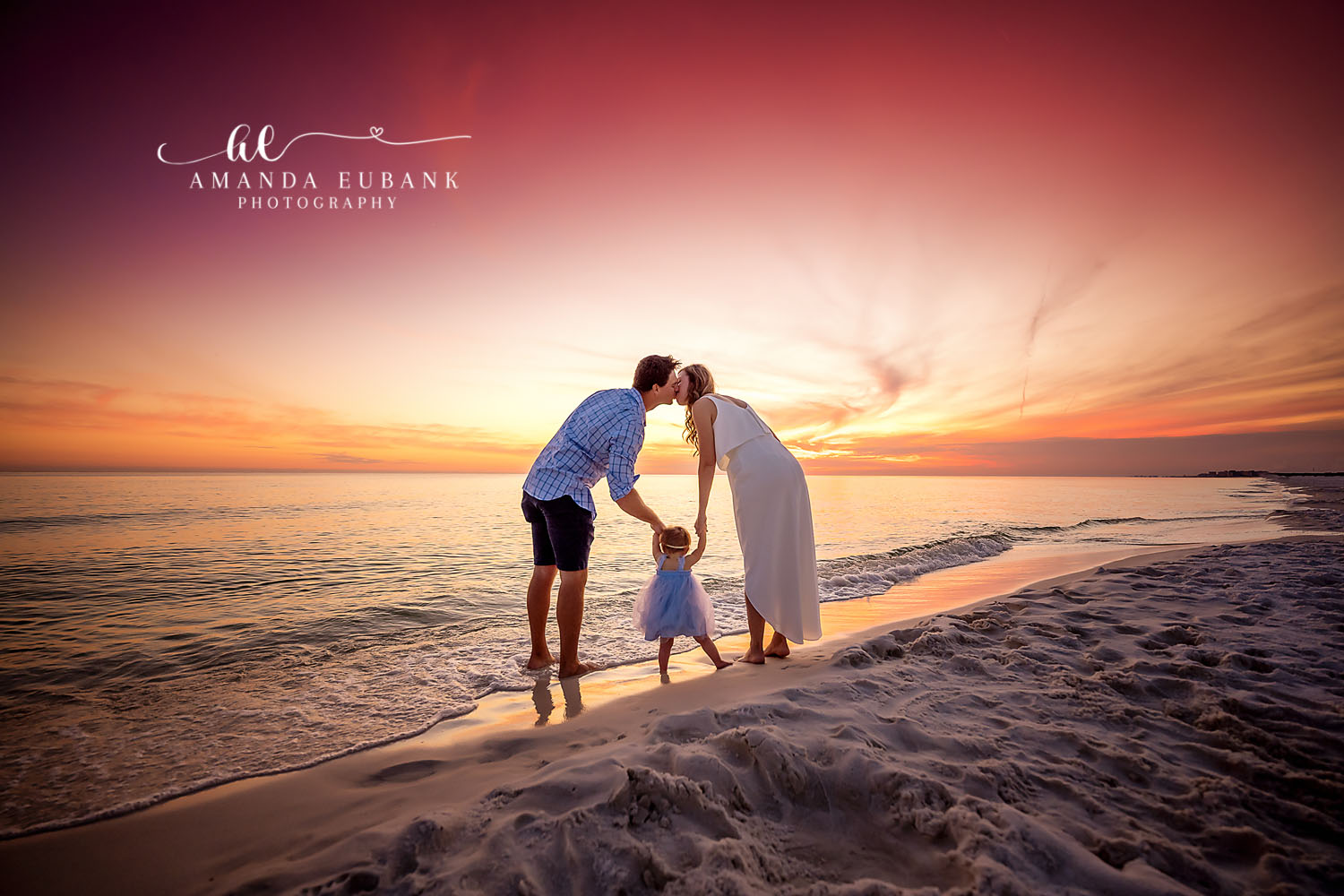 Kiss Over the Toddler | Tampa Beach Family Photography Tampa family photographer captures parents kissing above their toddler at the water's edge at golden hour.