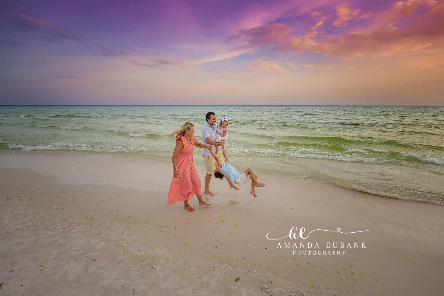 Swinging Through the Surf — Tampa, FL Family Session Parents swinging their child between them through the surf at dusk at a beach family session near Tampa, Florida.
