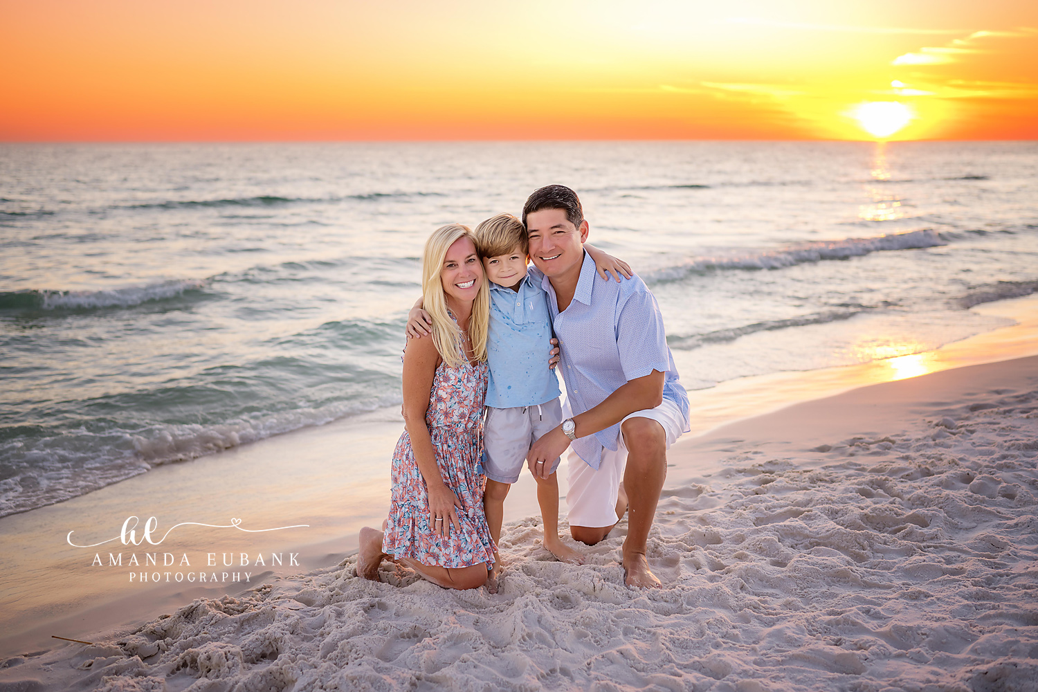Family of Four in Blue | Tampa Beach Family Photography Tampa family photographer captures a family of four sitting on the sand in blue and white with the sun setting behind.