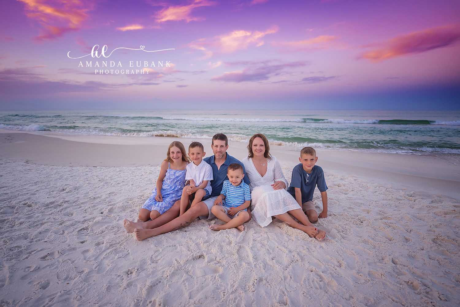 Family of Six in Blue Plaid — Tampa Bay Family Portraits A family of six seated on the sand in blue plaid and white under a purple sky — beach family photography in Tampa Bay.