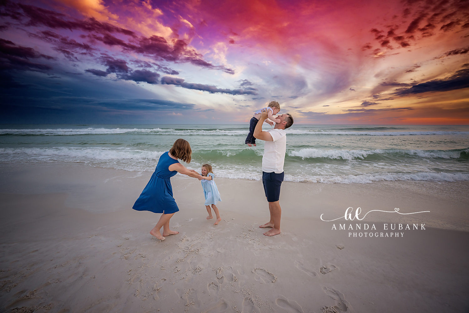 Parents and Toddlers at Sunset | Tampa Beach Family Photography Tampa family photographer captures parents lifting their toddlers on the beach under a dramatic purple cloudscape.