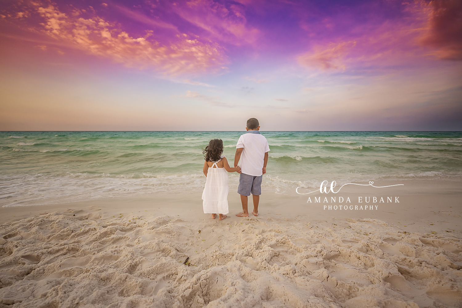 Two Kids at the Water’s Edge | Tampa Children’s Photographer Two children standing hand in hand at the water's edge beneath a purple sky during a children’s portrait session in Tampa, Florida.