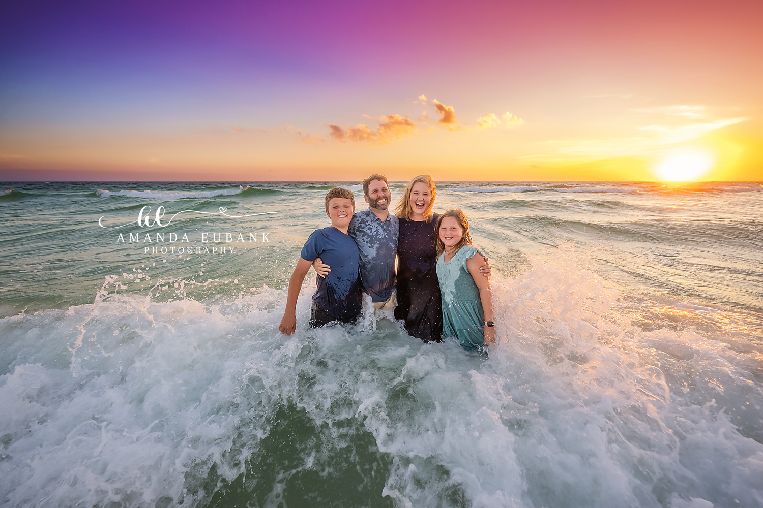 Family in the Breaking Waves | Family Photographer in Tampa, Florida Family beach portraits in Tampa, FL showing a family of five standing in breaking waves as the sun burns low on the water.