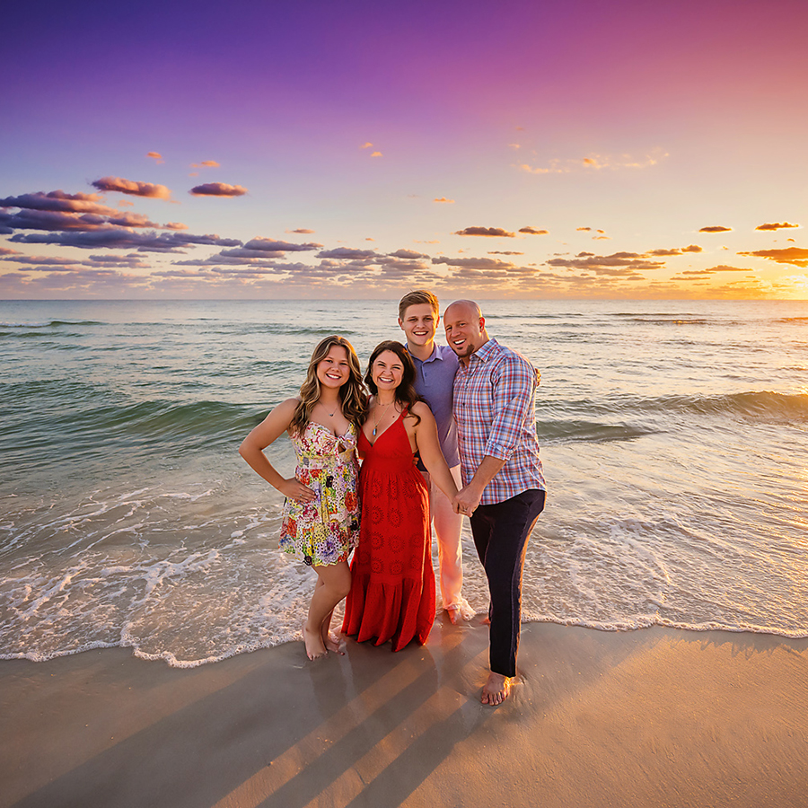 Family of Four in Red — Tampa Bay Family Portraits A family of four standing on the wet sand with mom in a red dress at dusk — beach family photography in Tampa Bay.