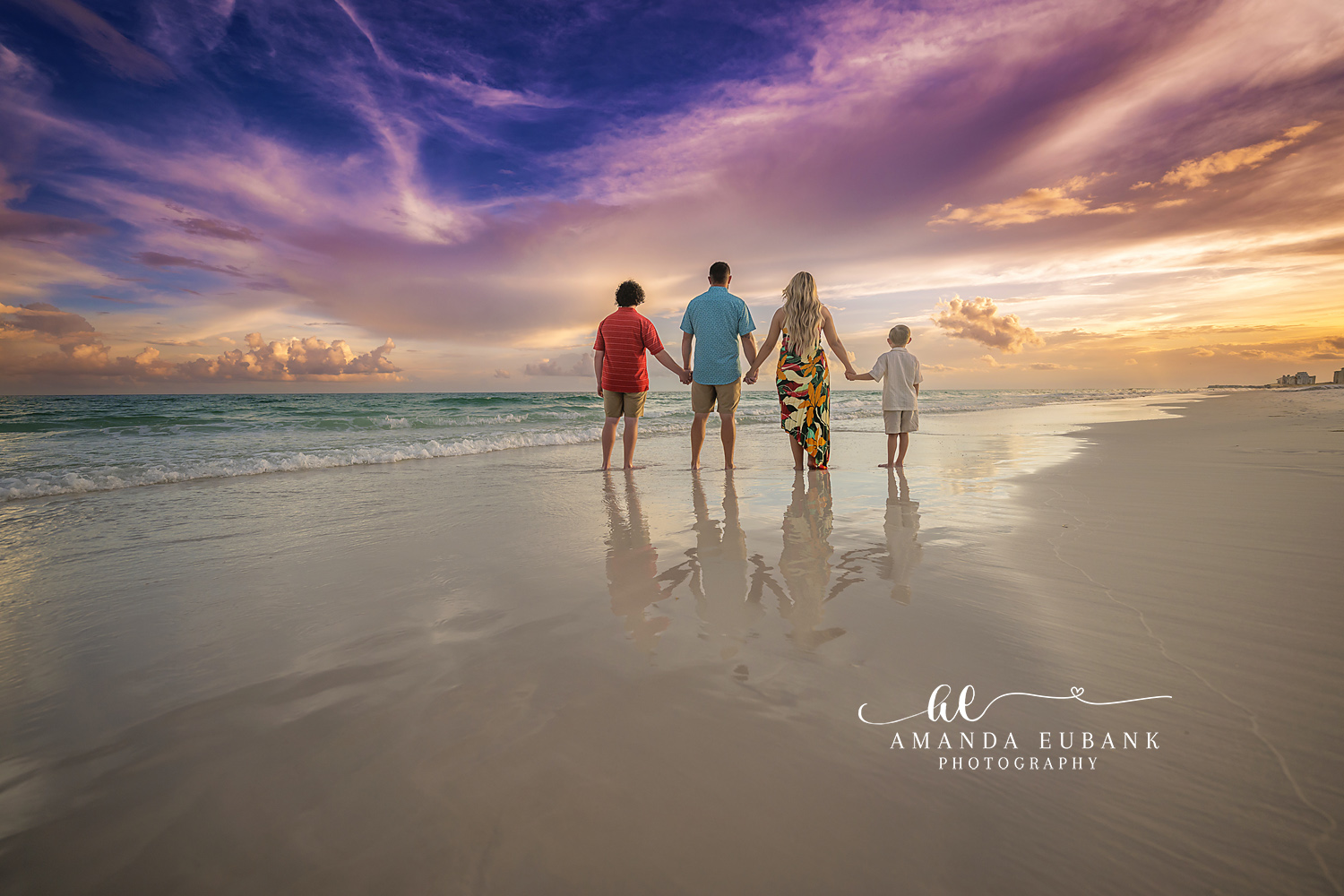Family Silhouette on Wet Sand | Family Photographer in Tampa, Florida Family beach portraits in Tampa, FL showing a family of four silhouetted on mirror-wet sand beneath a purple cloudscape.