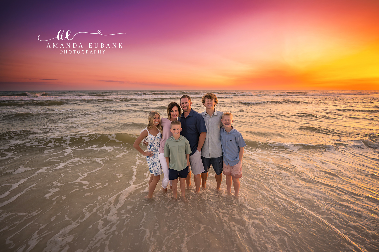 Family of Six in the Surf — Tampa, FL Family Session A family of six standing in the shallow surf under a blazing orange sky at a beach family session near Tampa, Florida.