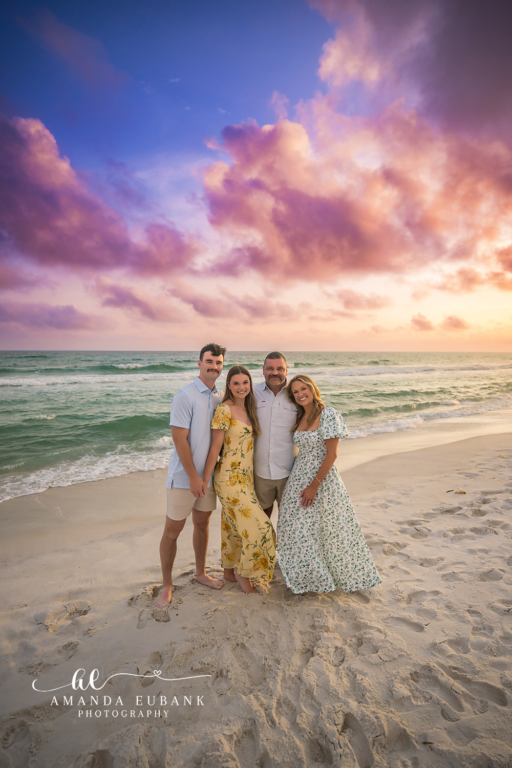 Family Portrait Under Purple Clouds — Tampa, FL Family Session A family of four on the beach in florals beneath billowing purple clouds at a beach family session near Tampa, Florida.