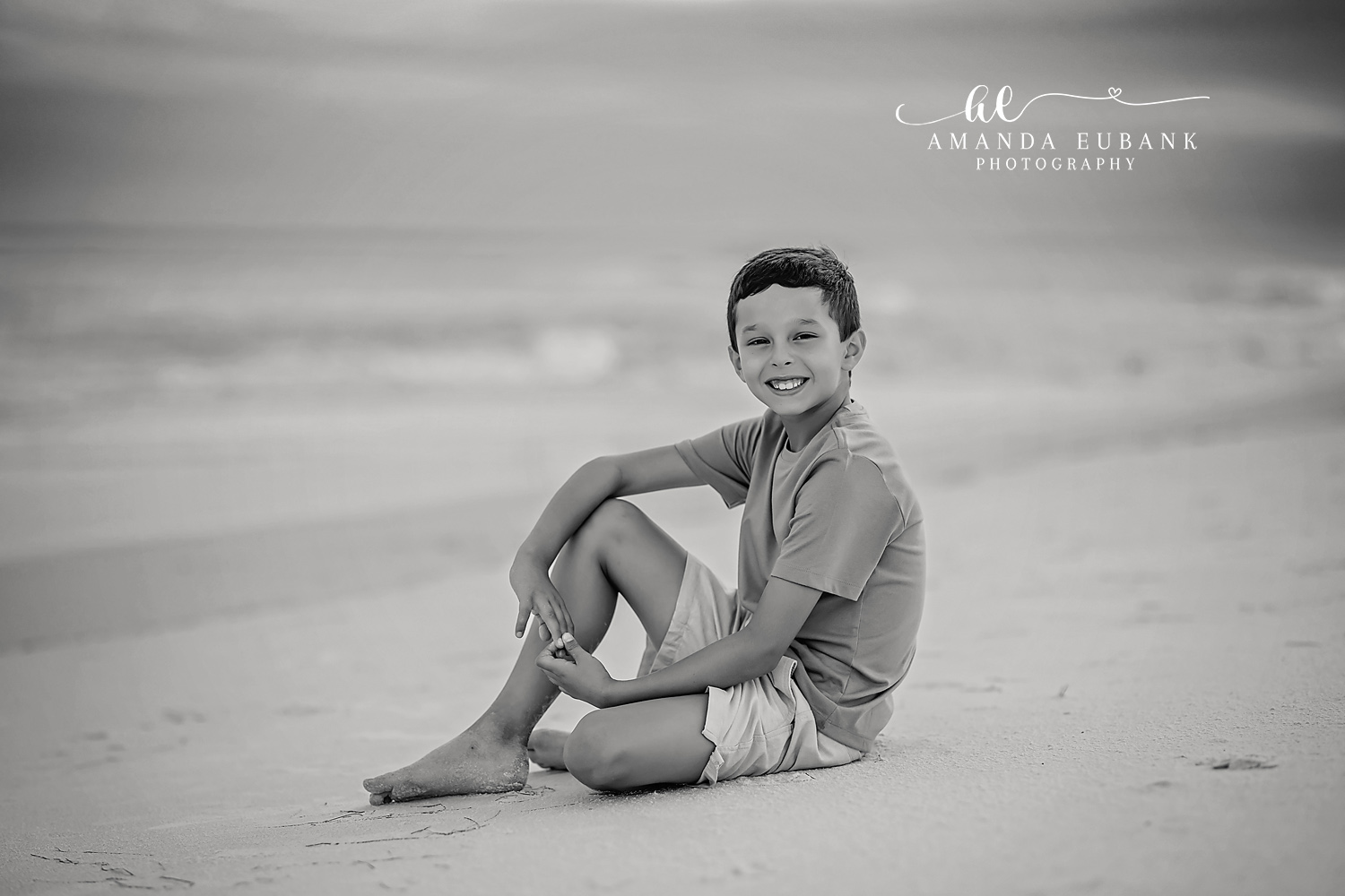Black and White Boy Portrait | Kids Beach Portraits in Tampa, FL Tampa children’s photographer captures a black and white portrait of a boy sitting on the sand hugging his knees.