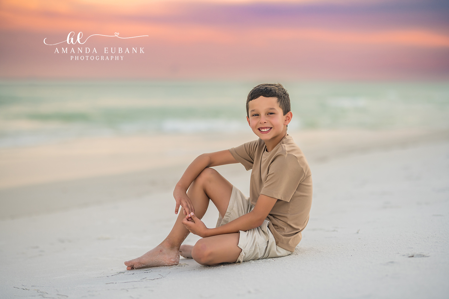 Boy on the Sand at Sunset — Tampa Bay Children’s Photography A young boy sitting on the sand in tan under a pastel pink sky at a beach kids session in Tampa, FL.