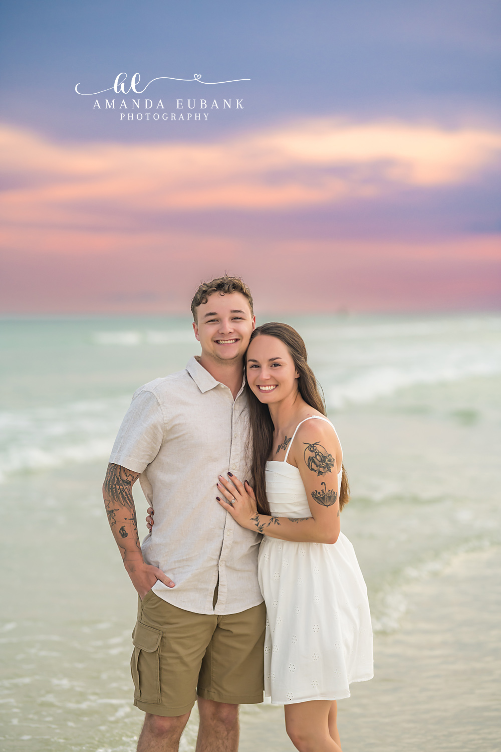 Couple in White at the Water — Tampa, FL Couples Session A couple standing in the shallow water in white beneath a pastel sky at a beach couples session near Tampa, Florida.