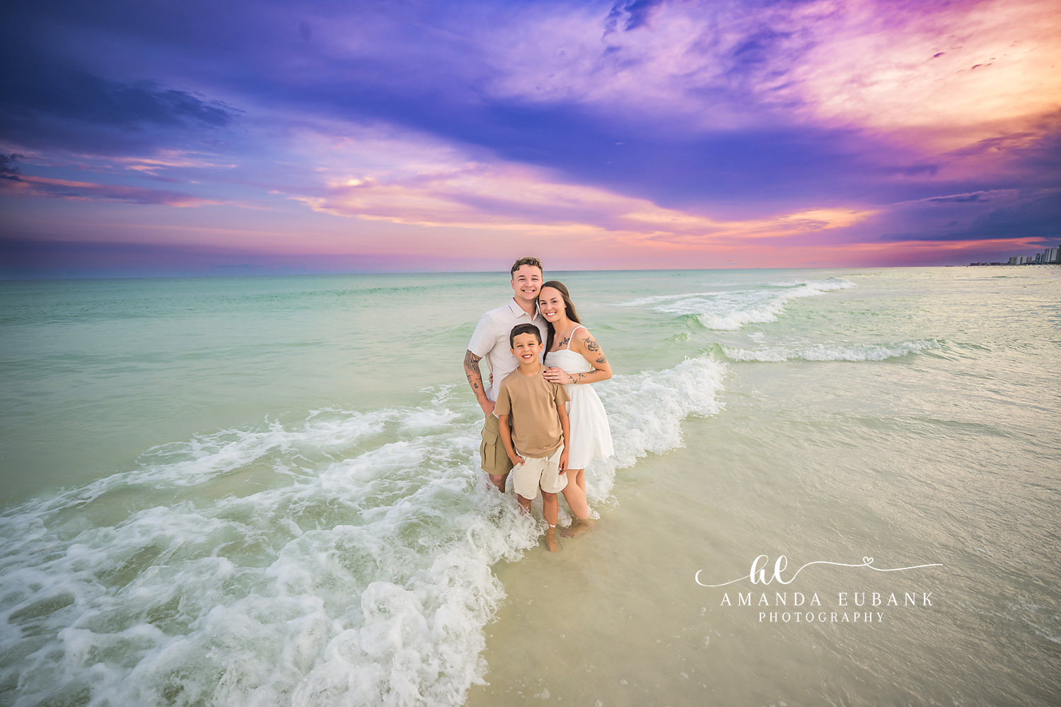 Family Kneeling in the Surf — Tampa Bay Family Portraits A family of three kneeling in the breaking surf beneath a purple cloudscape — beach family photography in Tampa Bay.